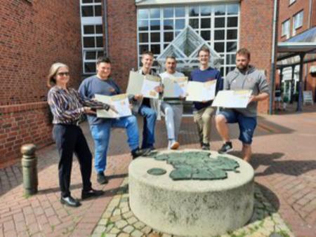 Fünf Bürger halten ihre Urkunden hoch, stehen im Halbkreis vor dem Rathaus.